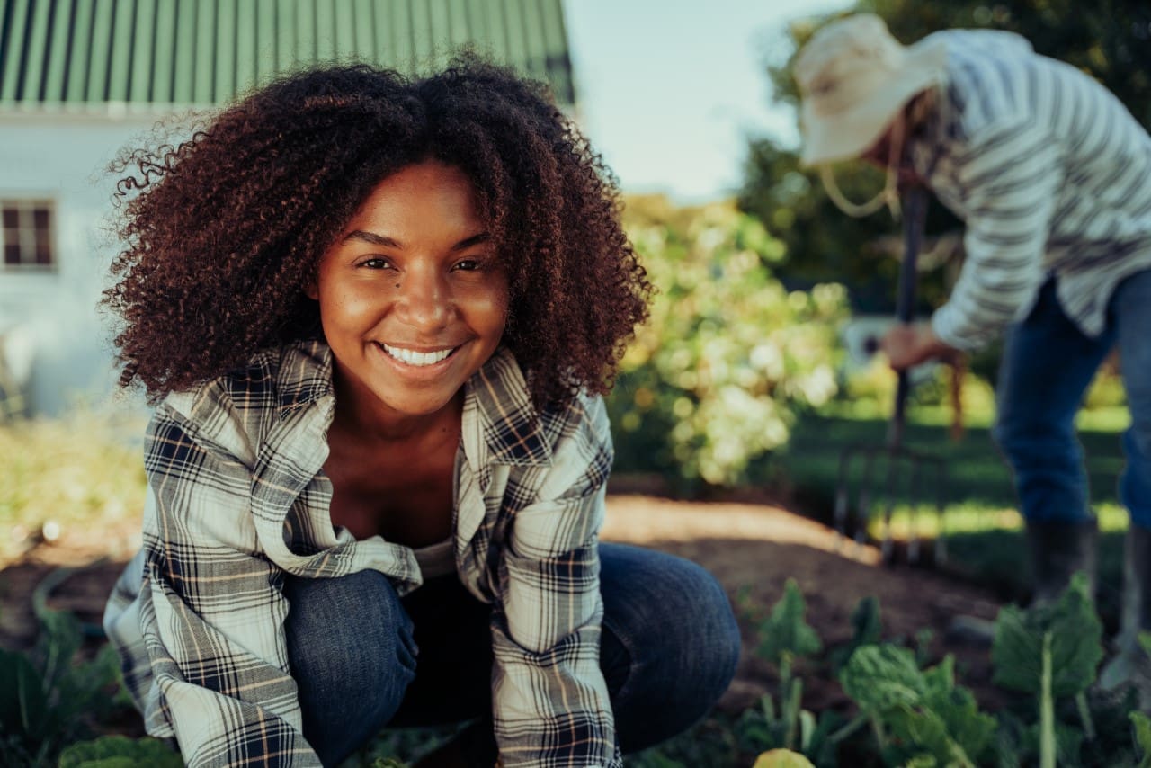 Beautiful smiling female farmer working in vegetable garden organising produce feeling active while working male friend digging holes. High quality photo